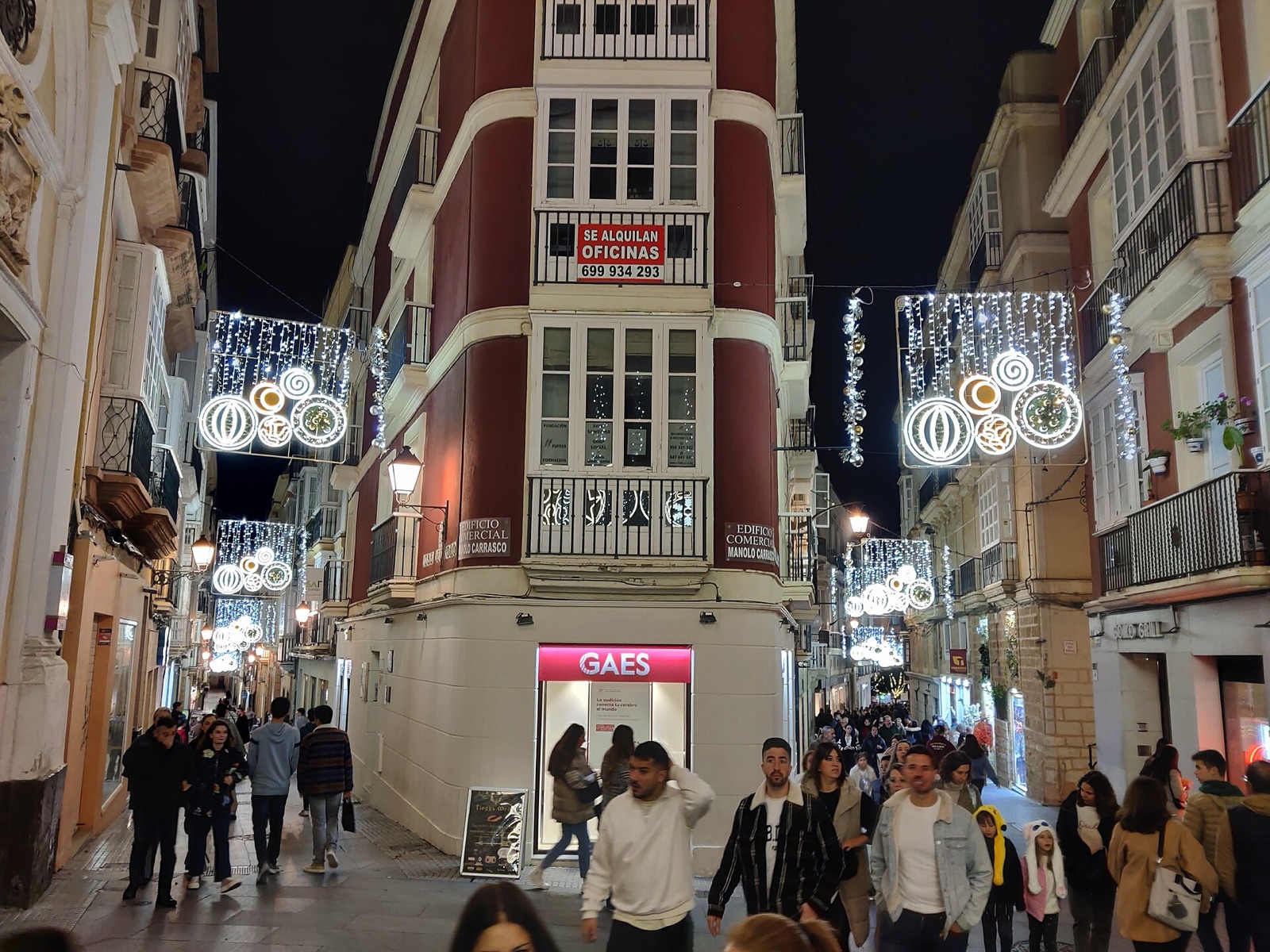 Calle comercial del casco antiguo de Cádiz con adornos de luces de Navidad y gente paseando, de noche