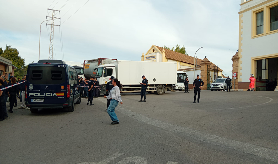 Varios policías y un furgón policial junto a camiones y edificios industriales, con personas en la calle.