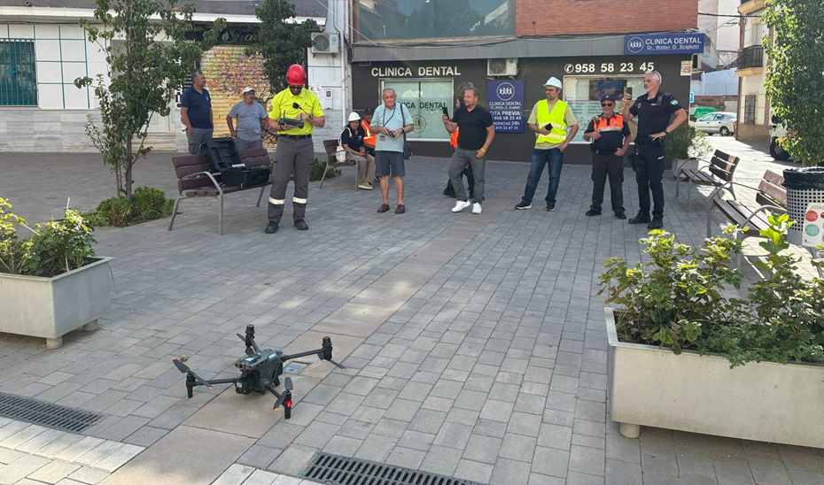 Un dron en el suelo de una plaza adoquinada y varias personas alrededor, algunas con chalecos y cascos, junto a una clínica dental.